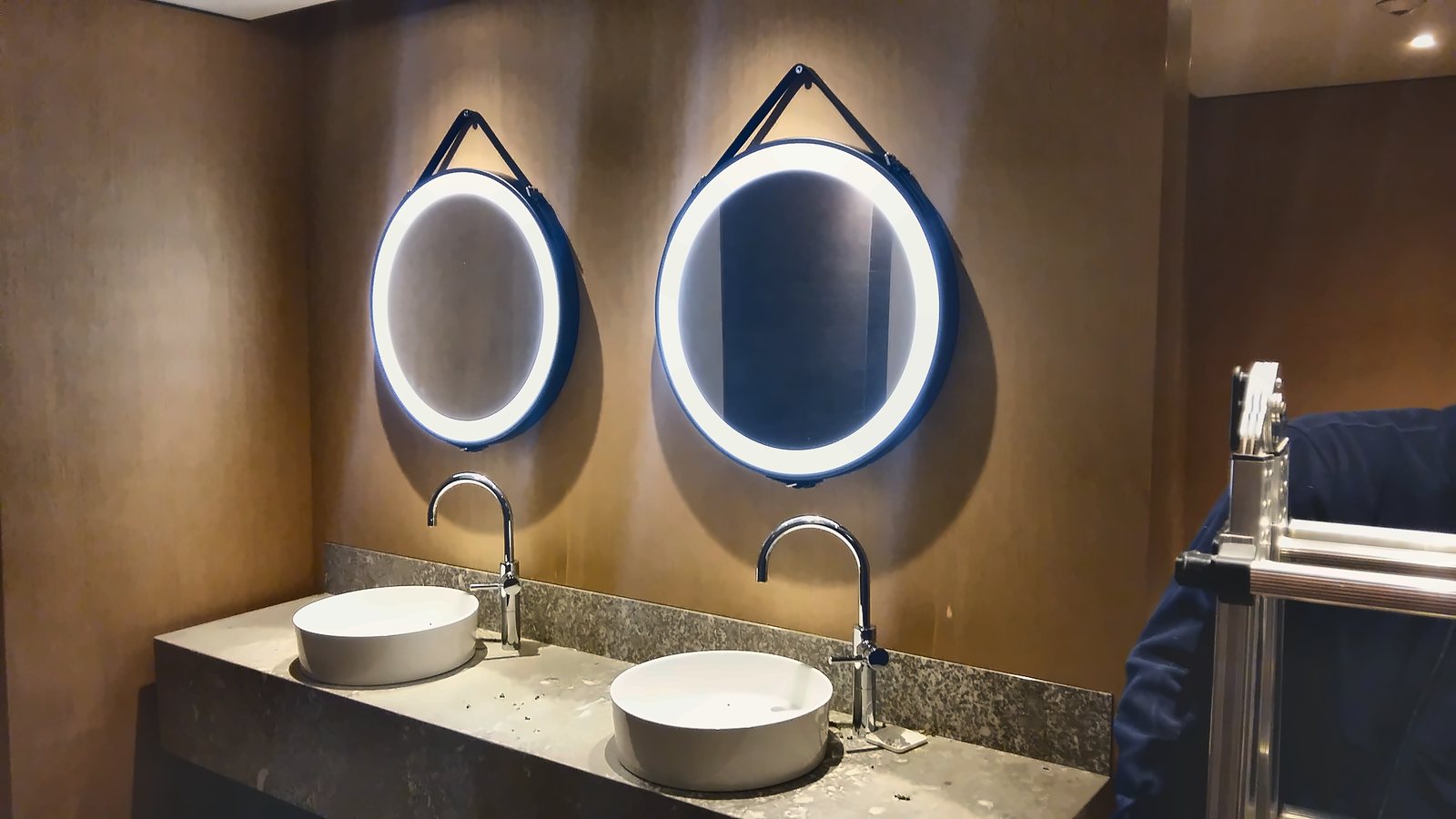 Two backlit circular mirrors hung on straps above the bathroom basins