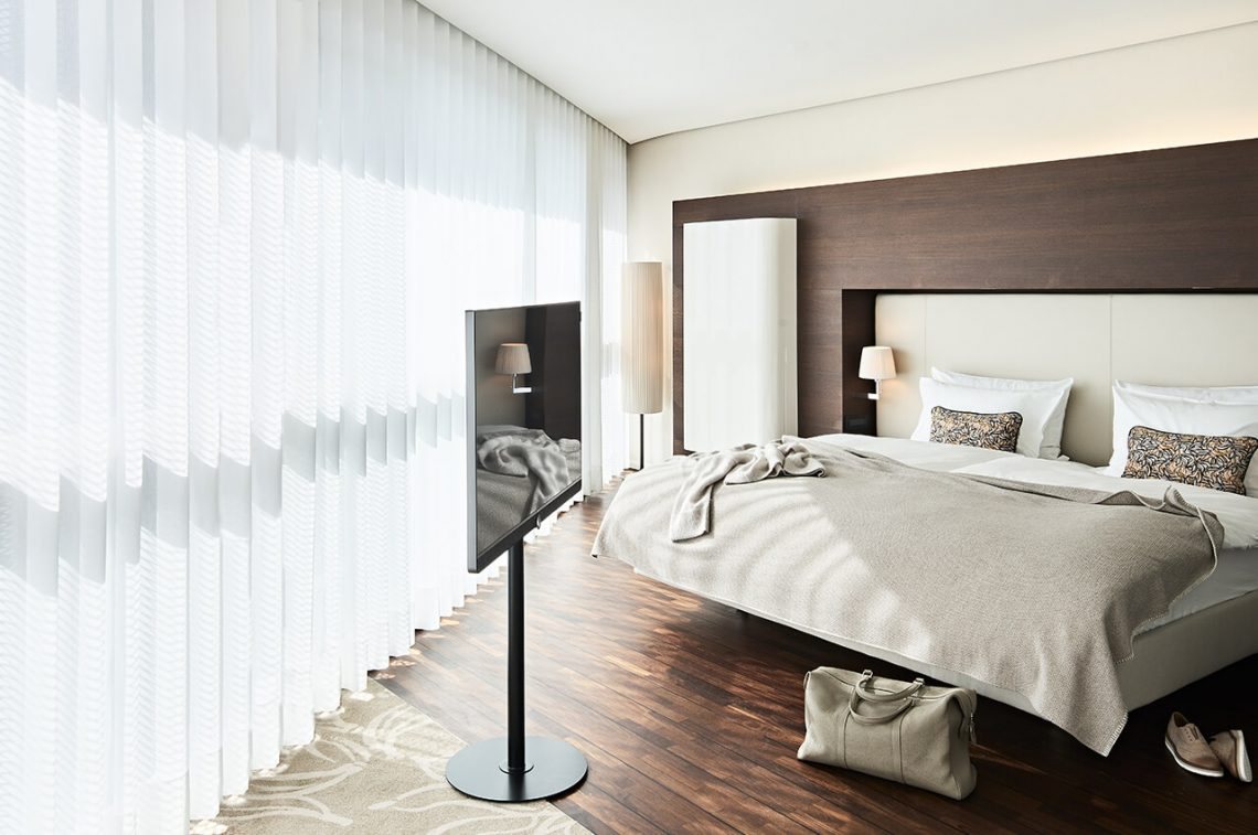 The cylindrical floor lamp beside the headboard, in the room with the full-width curtain wall