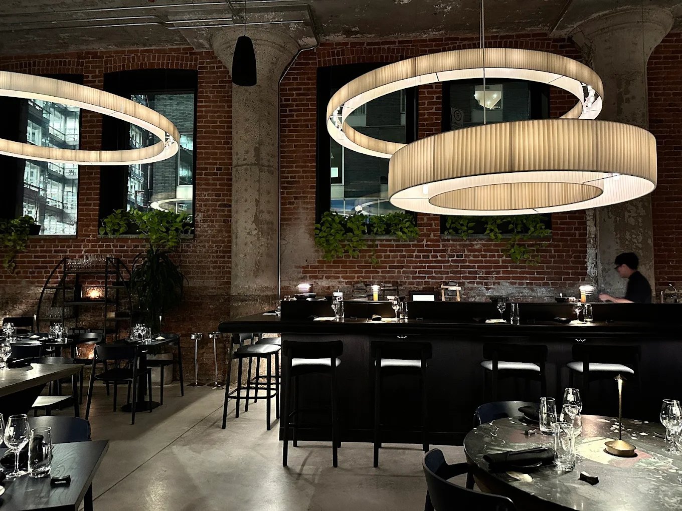 The NAMA Omakase dining room in Montreal: three pleated rings above the counter, between the columns and the brick wall