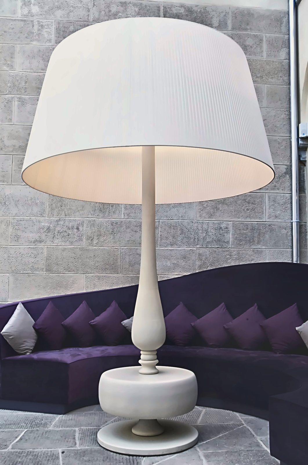 The Villa Le Maschere lobby floor lamp: turned wooden stem and wrapped conical shade, beside the curved sofa