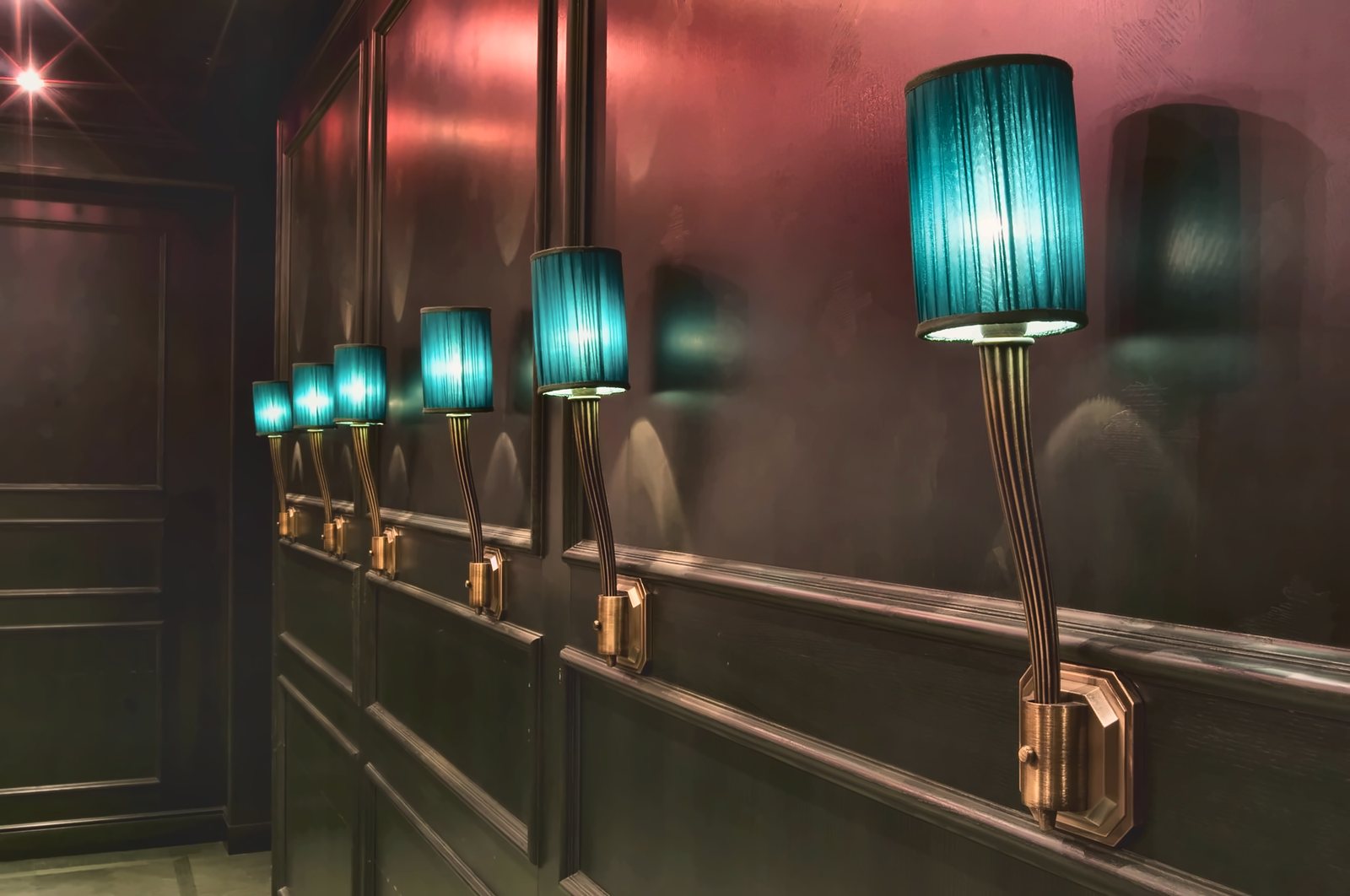 The row of turquoise pleated wall lights on brass arms and backplates, along the dark panelling
