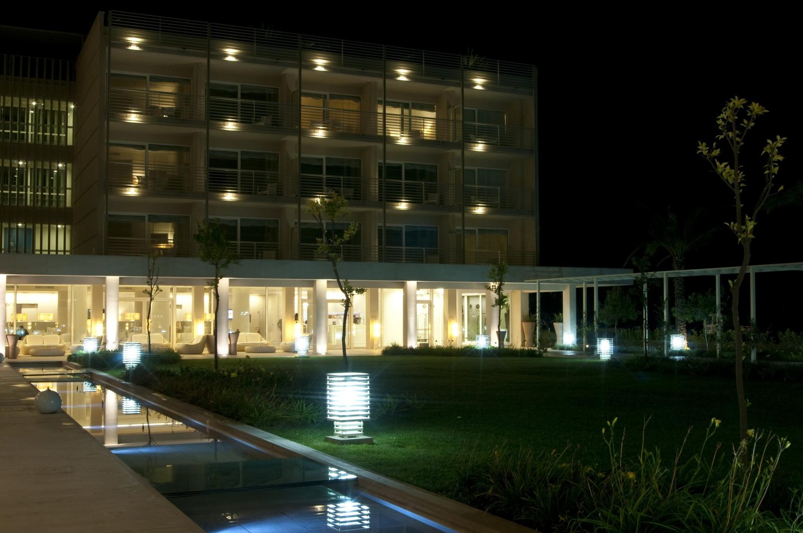 The hotel facade at night, with the reflecting pool in front and a slatted bollard lit on the lawn