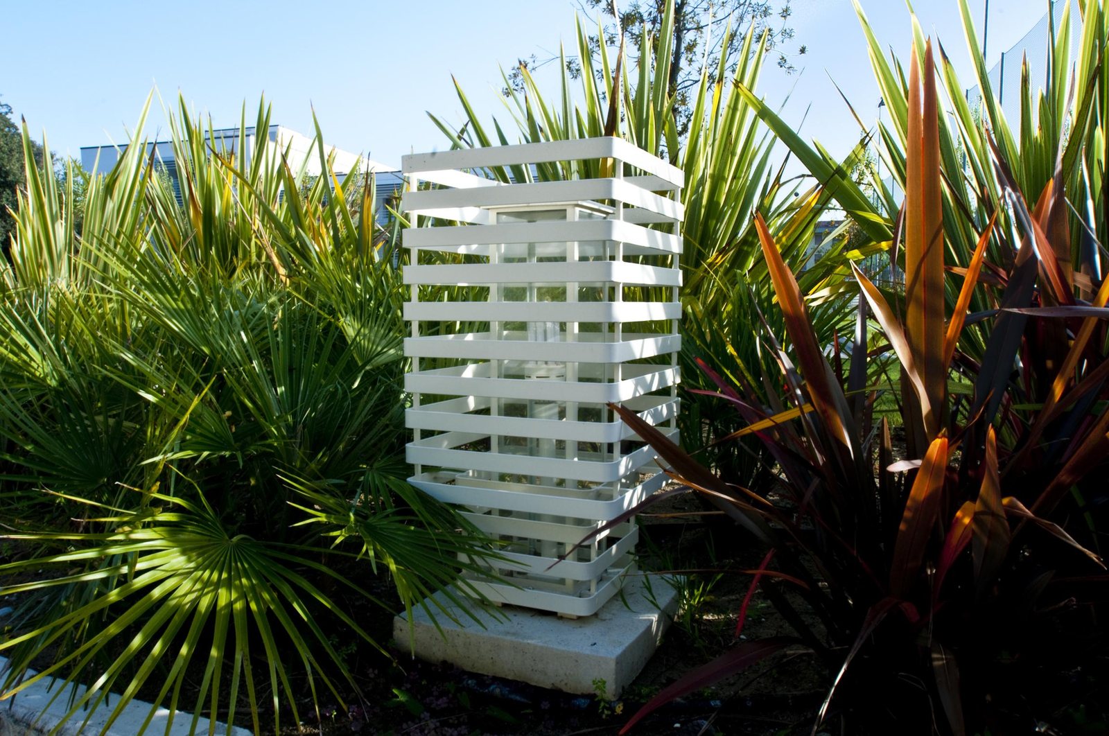 The white slatted bollard among the palm fronds and cordylines of the garden