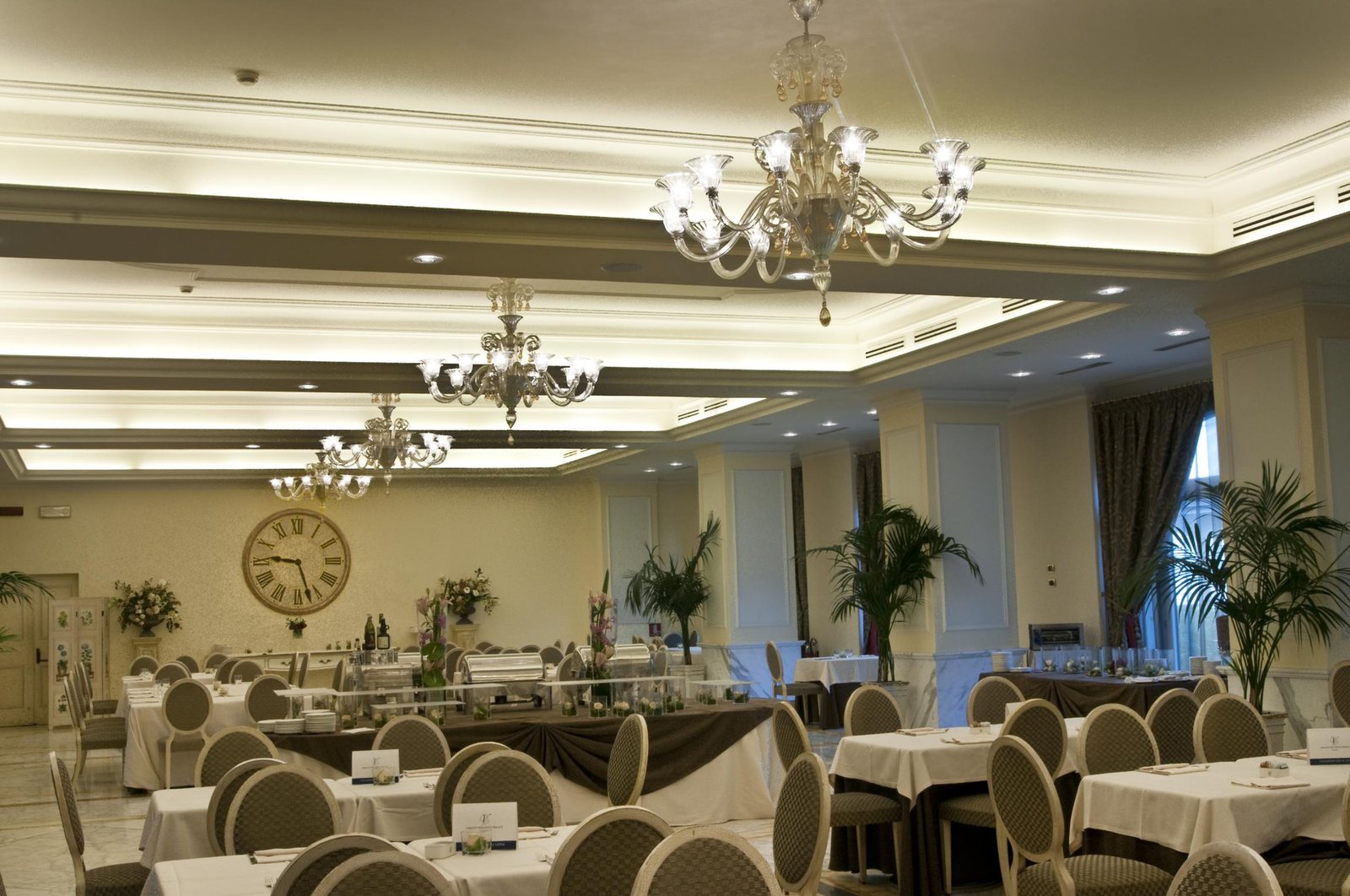 The banqueting room laid for service, blown glass chandeliers aligned under the coffered ceiling