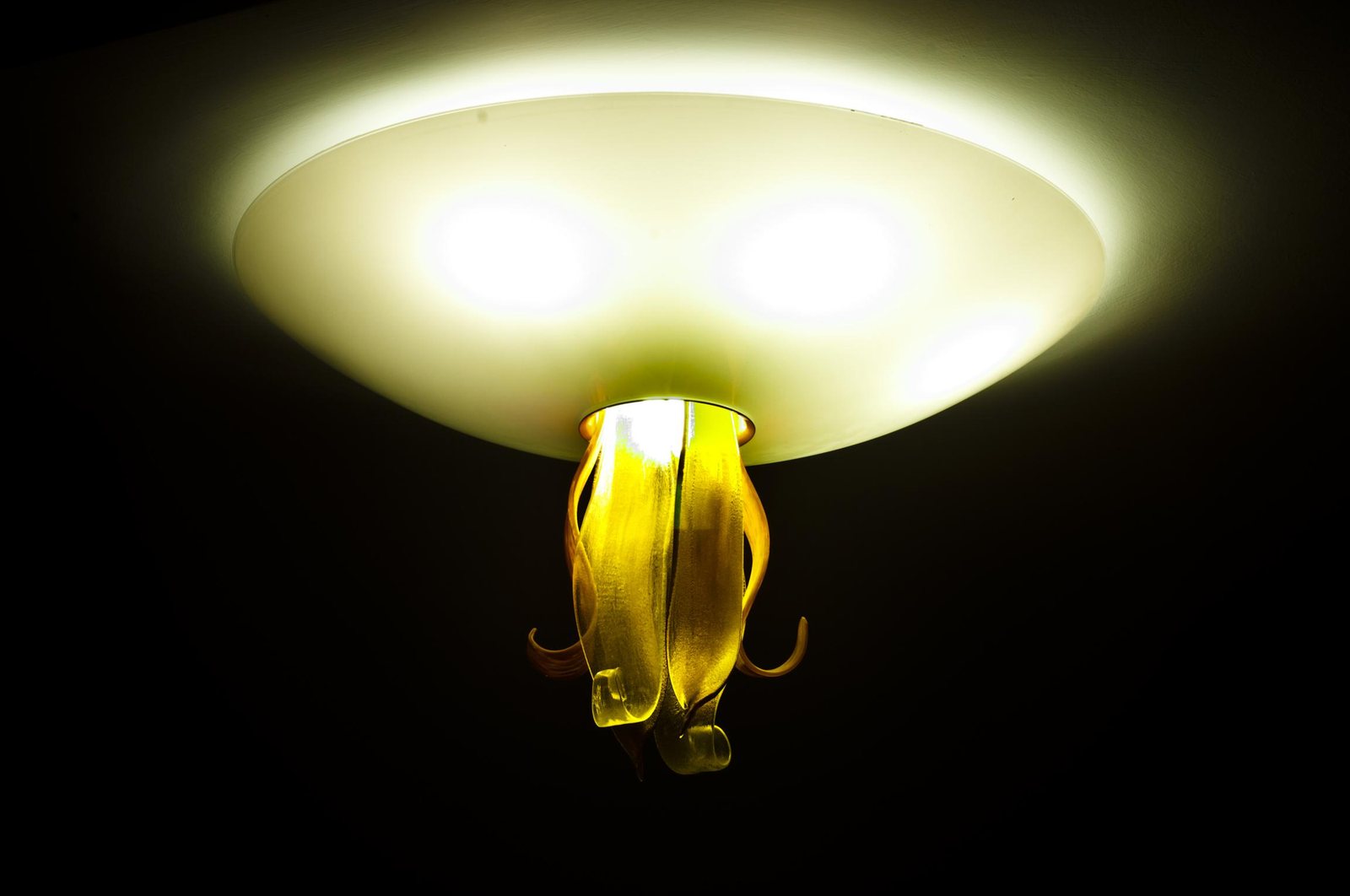 The opal glass bowl lit, with the amber glass flower hanging at its centre