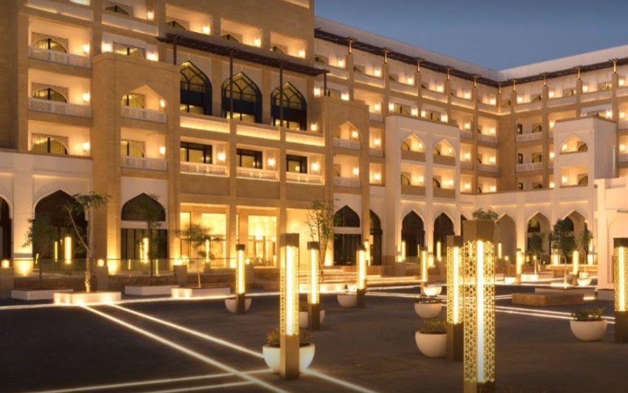 The courtyard at dusk, gilded perforated columns lit among the planters