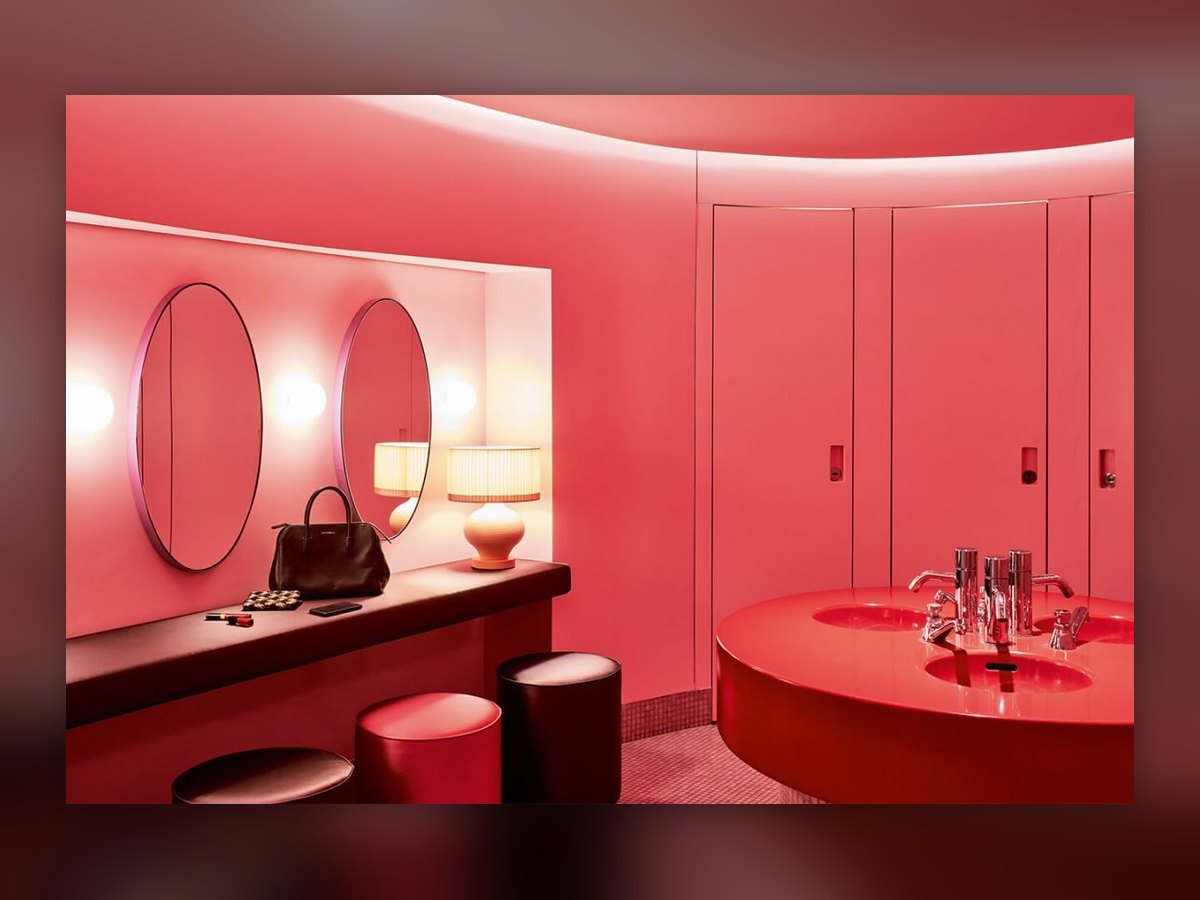 Two pleated-shade table lamps on the red bathroom counter, between the oval mirrors