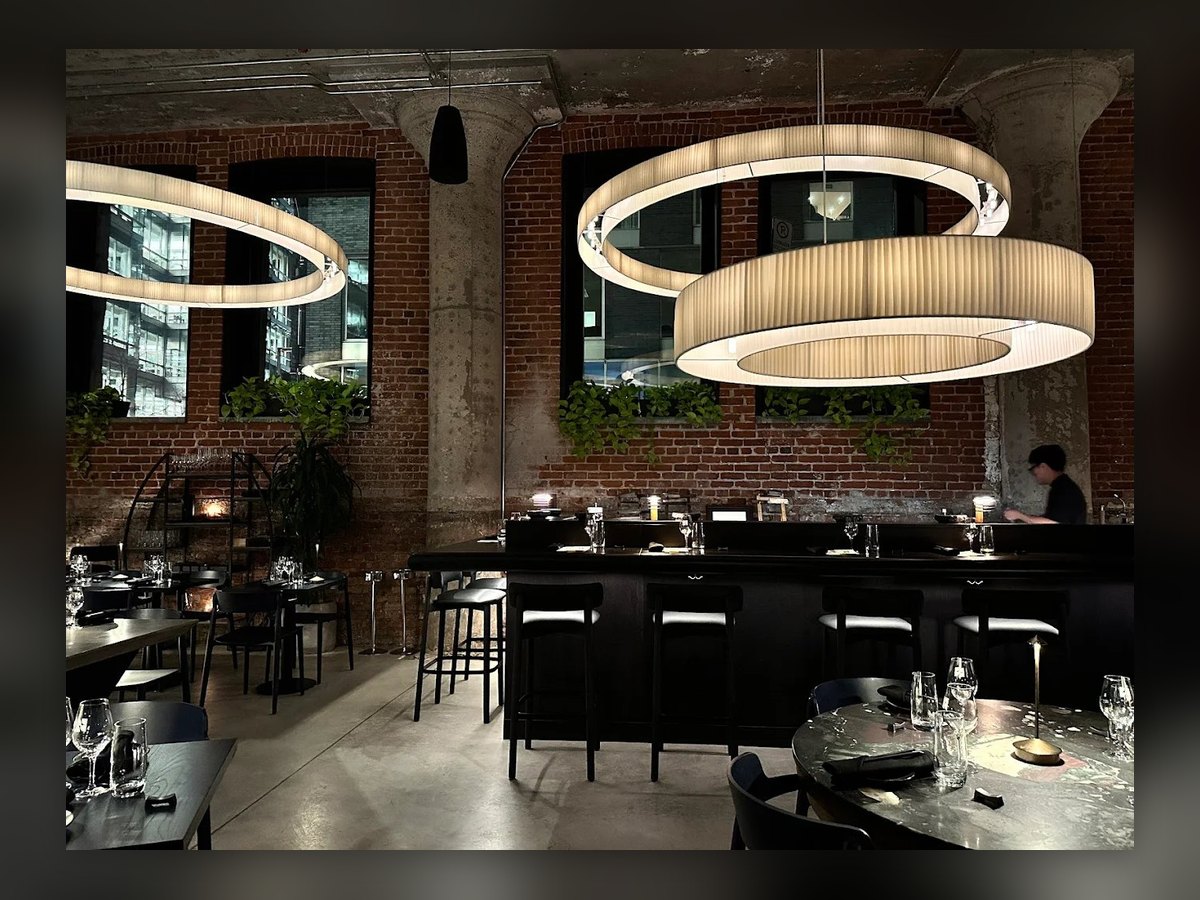 The NAMA Omakase dining room in Montreal: three pleated rings above the counter, between the columns and the brick wall