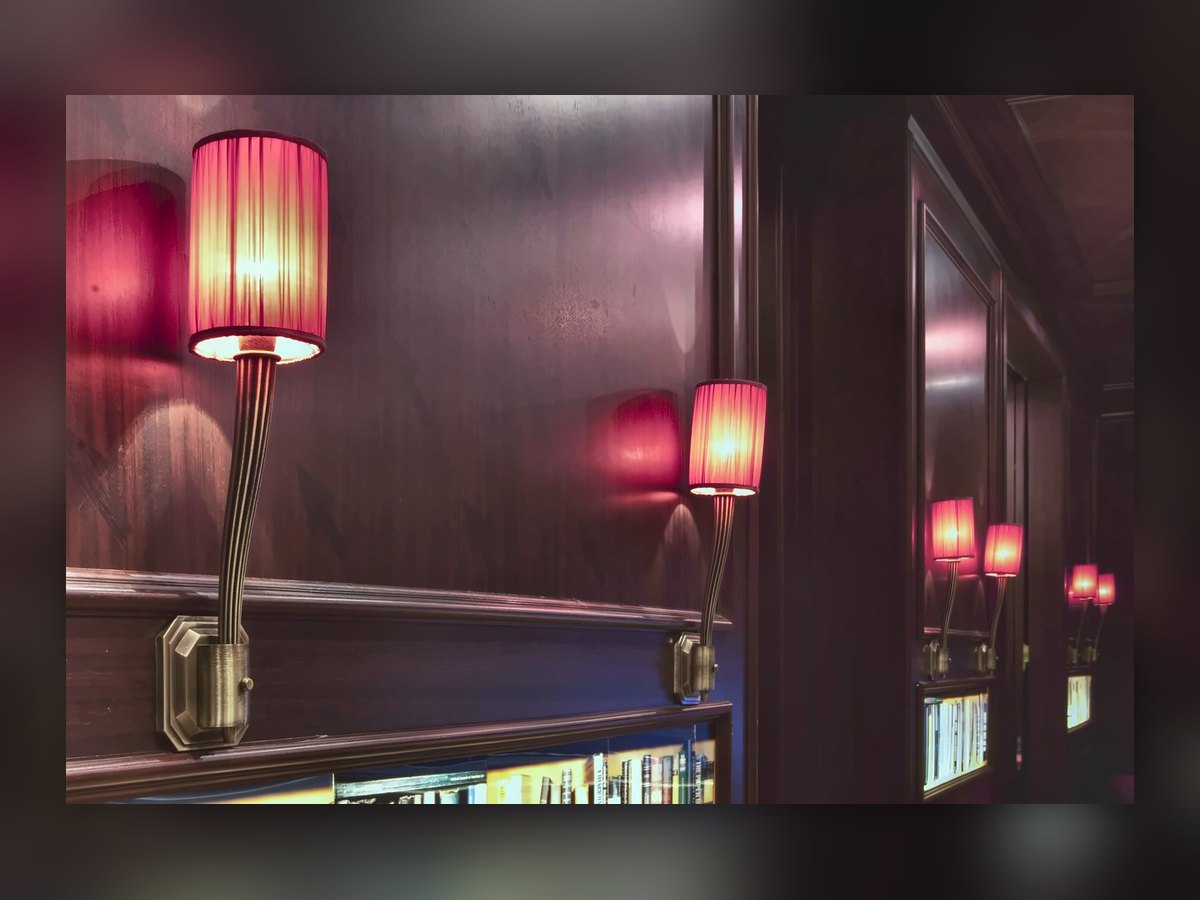 The red-shaded wall lights reflected in the corridor mirror, above the book niches