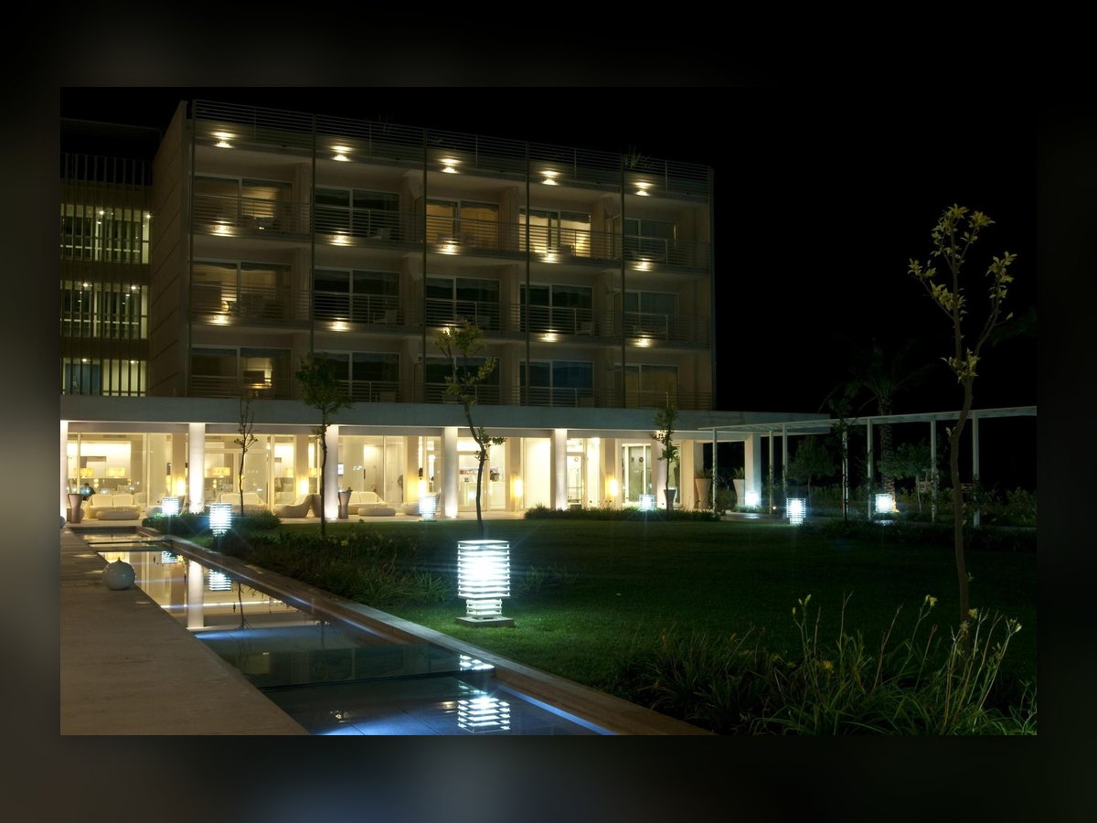 The hotel facade at night, with the reflecting pool in front and a slatted bollard lit on the lawn