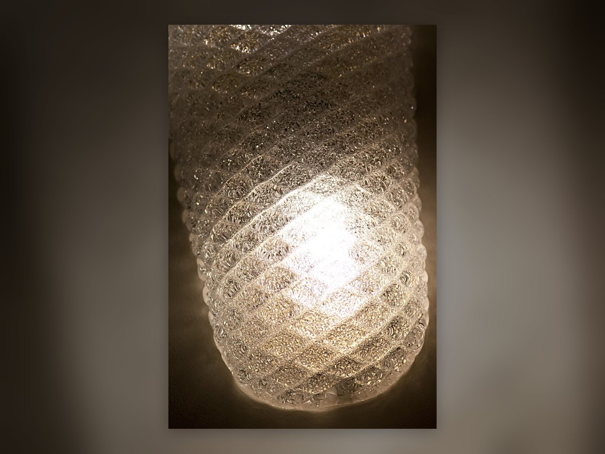 A detail of the lit spiral-ribbed glass, its texture readable through the light