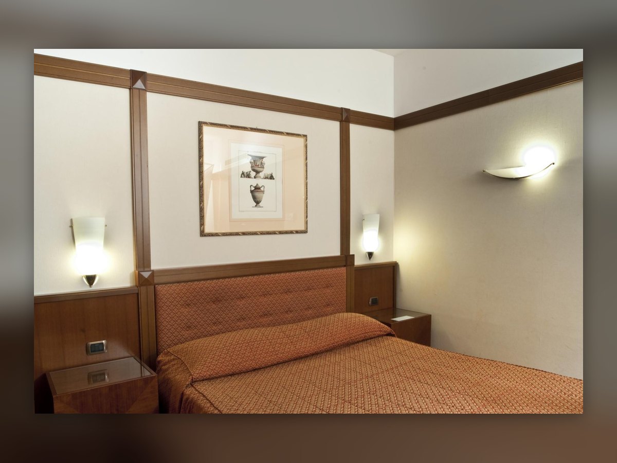 The guest room with wall lights lit either side of the bed and another on the far wall