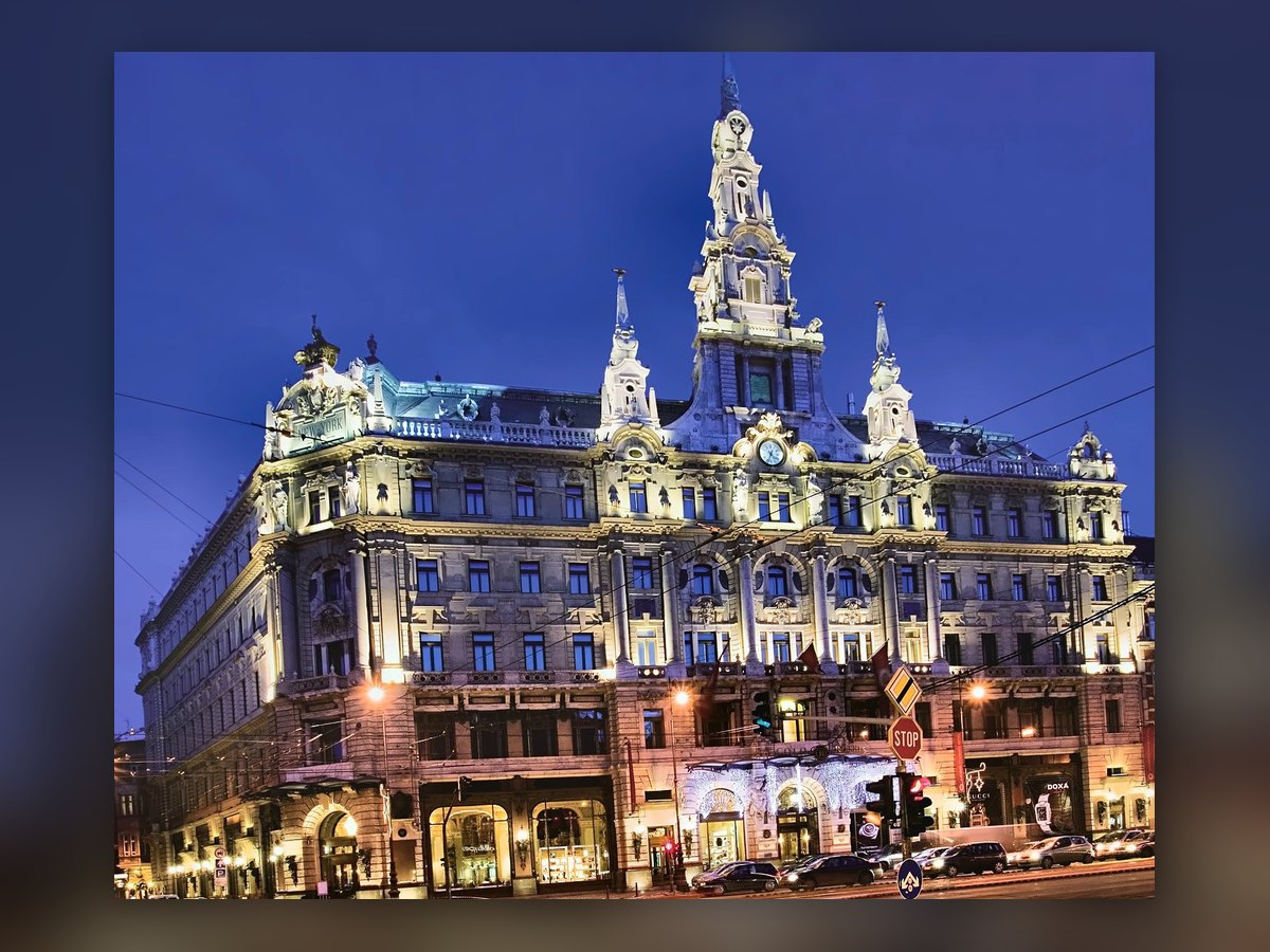 The New York Palace in Budapest lit up under a deep blue sky: the central tower, the clock and the New York lettering on the corner gable