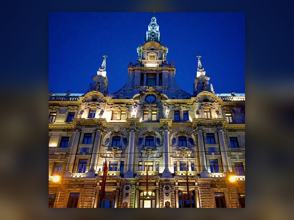 Der Mittelturm und die Fassade des New York Palace bei Nacht, von vorn gesehen: von unten beleuchtete Säulen und Gesimse